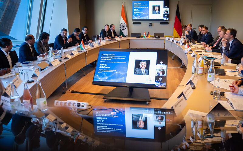 Zwei Personen stehen vor einer Präsentationswand zwischen der indischen und der deutschen Flagge und halten jeweils eine unterzeichnete Mappe in den Händen, was auf eine formelle Vereinbarung im Rahmen des deutsch-indischen Digitaldialogs hinweist.