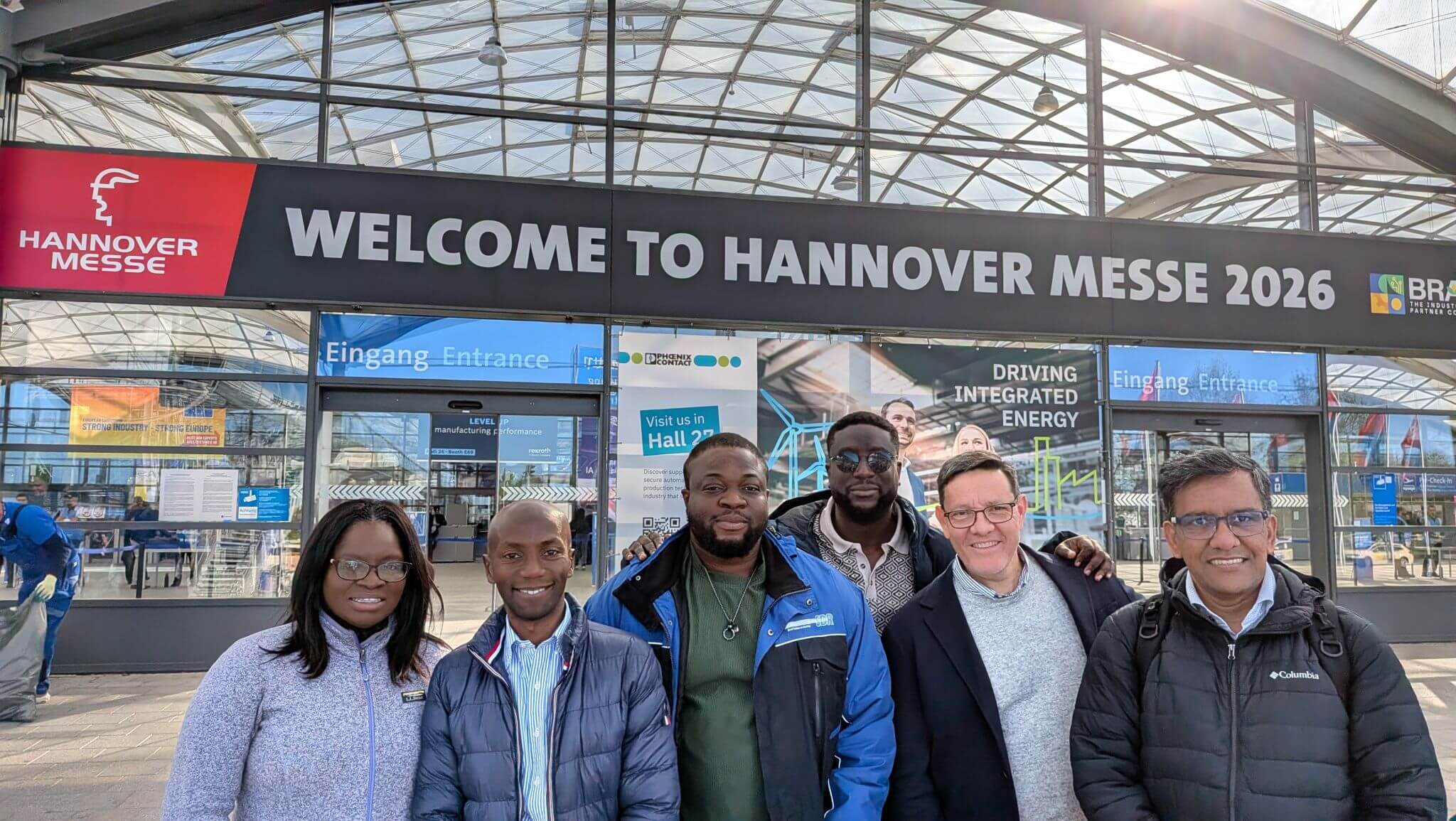 A group of six delegates poses in front of the main entrance of Hannover Messe 2026.